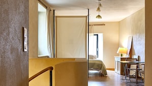 A spacious room with a wooden staircase, a bed, a desk, and a window with curtains. - The Studio (Valliguières)