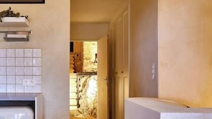 A narrow hallway with a kitchen area on the left, a stone wall in the background, and a door leading to another room. - The Studio (Valliguières)