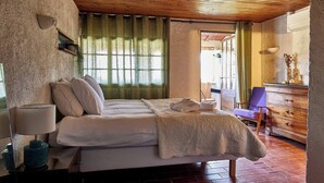 A bedroom with a wooden ceiling, a bed with white linens, a dresser, and a chair. - The Suite (Valliguières)