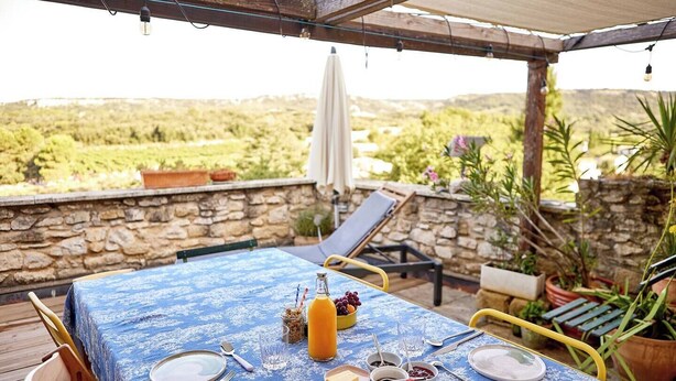 A table set for breakfast with a blue tablecloth, plates, cutlery, and a fruit bowl. - The Suite (Valliguières)