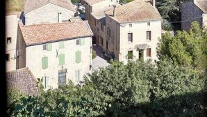 A cluster of traditional buildings with terracotta roofs, surrounded by lush greenery and hills in the background. - The Suite (Valliguières)