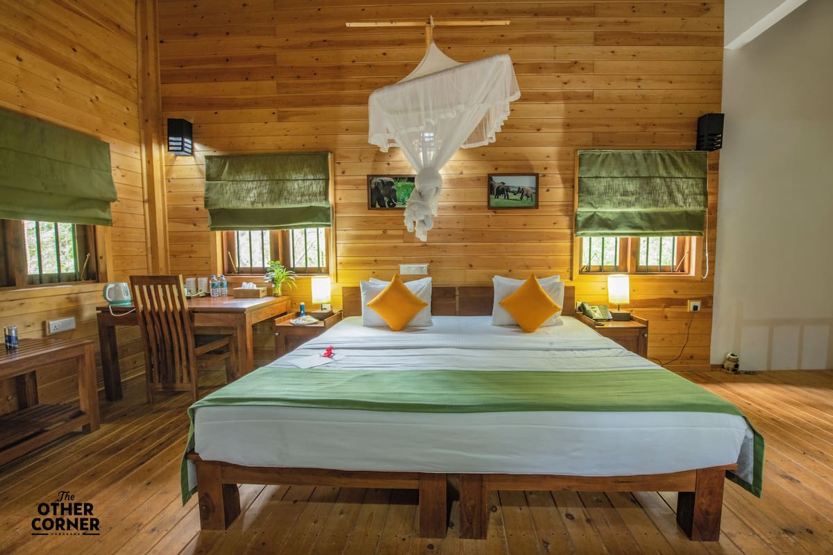 Una habitación de cabaña de madera con una cama grande, dos mesitas de noche, una silla y un escritorio con una lámpara.