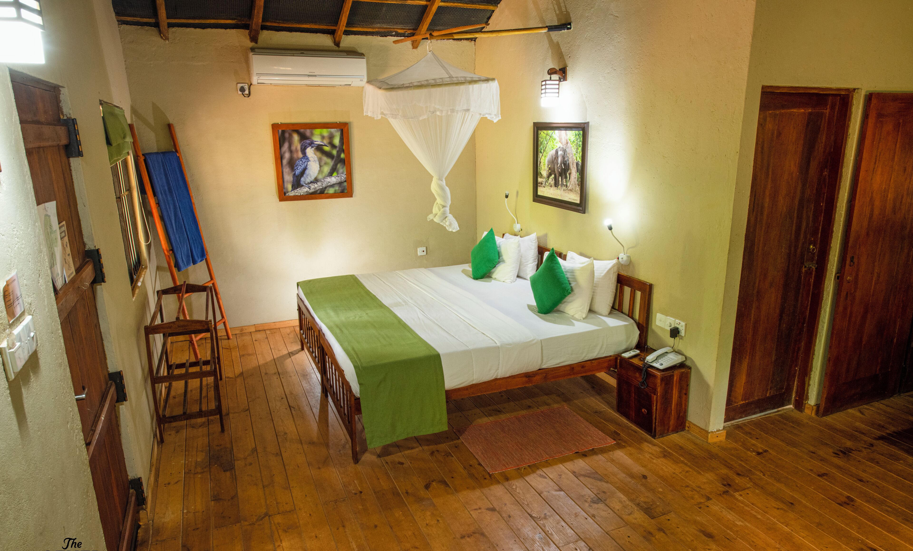 A wooden-floored bedroom with a bed, a standing fan, and a wall-mounted air conditioner.