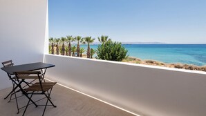 Een balkon met een tafel en stoelen, met uitzicht op de kust, palmbomen en de zee.