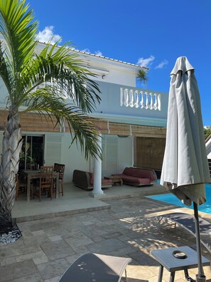 Ein Poolbereich mit Esstisch, Stühlen, einer Couch und einem Sonnenschirm.