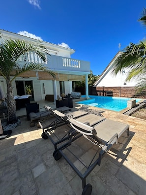 Ein modernes Haus mit Pool, Gartenmöbeln und einer überdachten Terrasse.