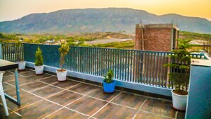 A balcony with potted plants, a view of distant mountains, and a brick structure.