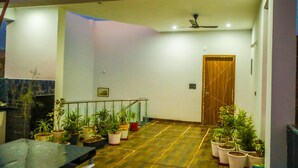 A spacious indoor area with a tiled floor, a ceiling fan, and several potted plants arranged along the walls.