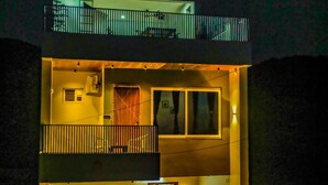 A two-story building with a balcony on the upper floor, a garage door, and a small outdoor area with plants.