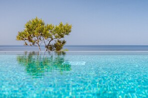 A tree-lined infinity pool with clear blue water reflecting the sky. - Terra Lucis Mountain Residences (Zakynthos)