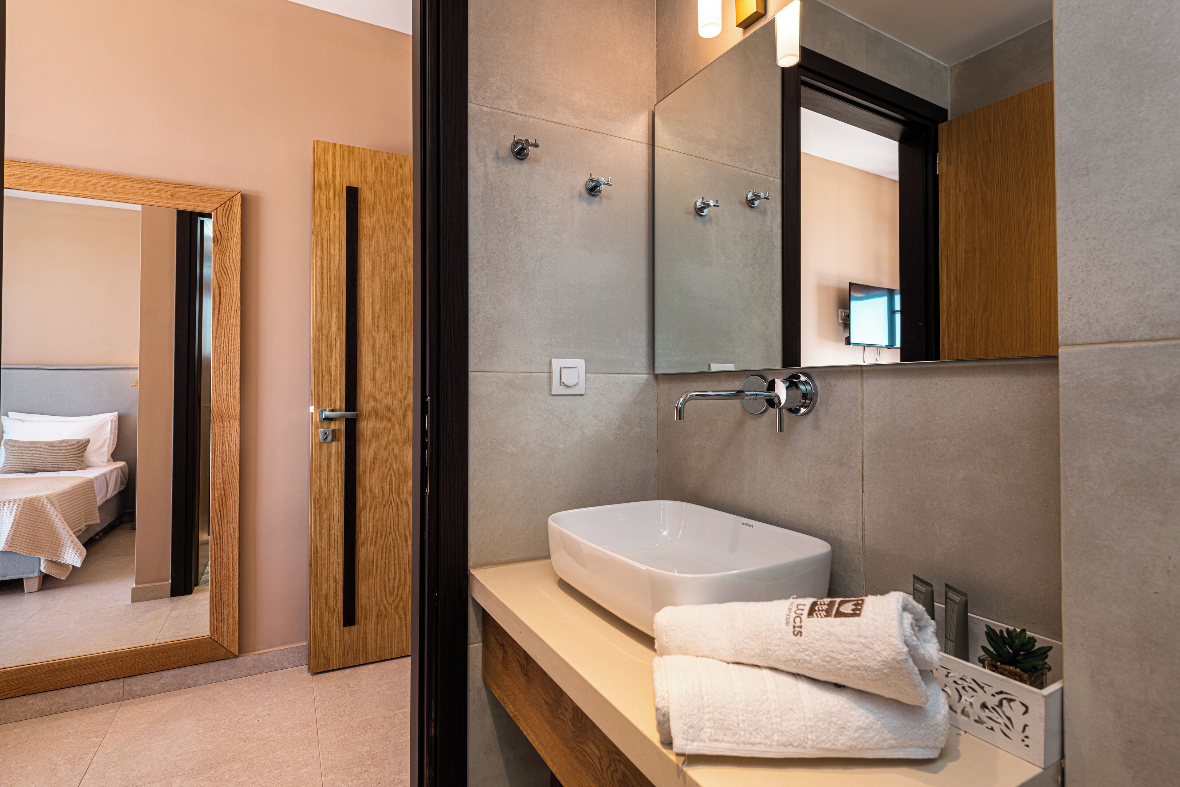 A modern bathroom with a large mirror, a sink, and a door leading to a bedroom.