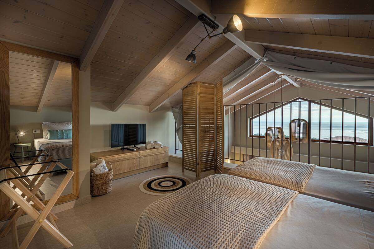 A modern bedroom with a large bed, a small desk, and a view of the sea.