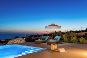 A poolside area with two lounge chairs, a small table, and a decorative umbrella. - Terra Lucis Mountain Residences (Zakynthos)