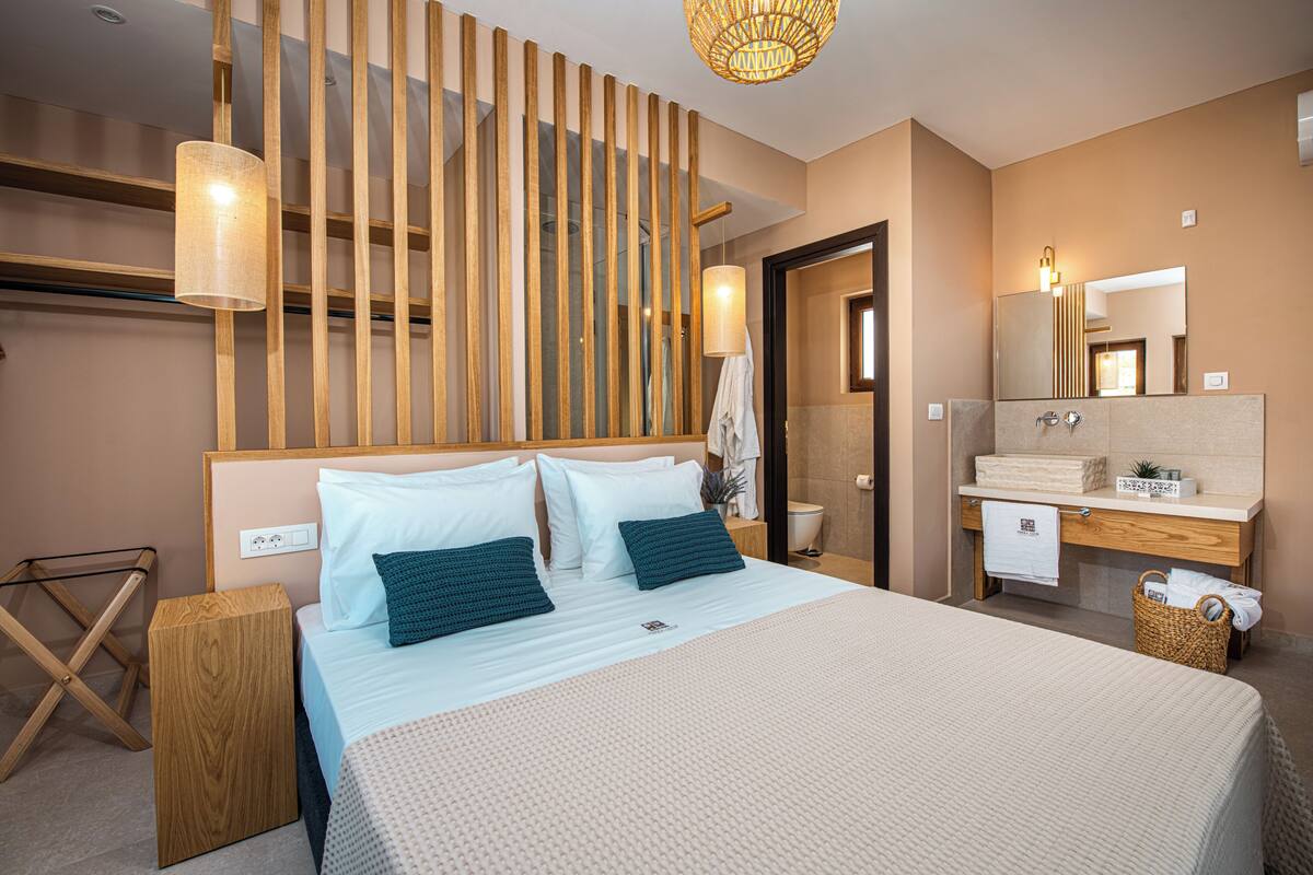 A modern hotel room with a large bed, wooden headboard, a wooden partition, a bathroom with a mirror, and a small wooden side table.