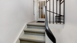 Una escalera con barandilla negra, paredes blancas y una puerta con paneles de vidrio esmerilado.