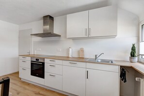 Une cuisine moderne avec des armoires blanches, une hotte en acier inoxydable, un four encastré et un plan de travail en bois.