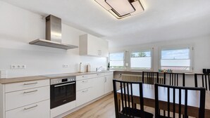 Una cocina moderna con armarios blancos, horno empotrado y comedor con mesa y sillas de madera.