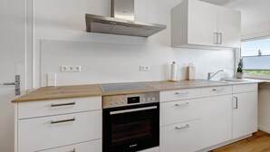 Una cocina moderna con armarios blancos, un horno Bosch, una campana extractora de acero inoxidable y un ventanal con vistas.
