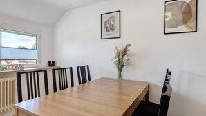 Un comedor con una mesa de madera, sillas negras, un florero con plantas secas y dos obras de arte enmarcadas en la pared.