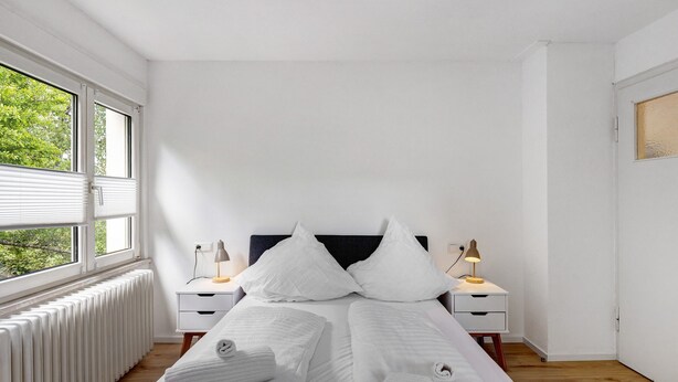 Un dormitorio con una cama, dos mesitas de noche, un radiador y una ventana con persianas.