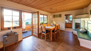 Un plafond en bois, un coin repas avec une table et des chaises, une cuisine et une vue à travers une porte vitrée.