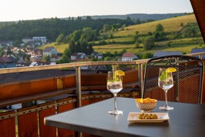 Een balkon met een tafel, twee glazen heldere drank met citroenpartjes, een schaal met snacks en een prachtig uitzicht over een dorp.