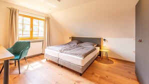 Une chambre à coucher avec un lit, une chaise, une table, une fenêtre et une lampe de chevet.