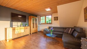 Un salon avec un plafond en bois, un canapé, un téléviseur, un meuble et une fenêtre donnant sur un beau paysage.