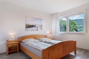 Un dormitorio con una cama de madera, dos mesitas de noche con lámparas, una ventana con vistas a árboles y un cuadro en la pared.