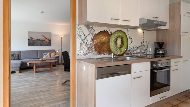 A modern kitchen with white cabinets, a dishwasher, an oven, and a countertop with a kiwi decoration. - Apartment "Haus Reiser" with Private Terrace, Garden, and Wi-Fi in Alpirsbach (Alpirsbach)