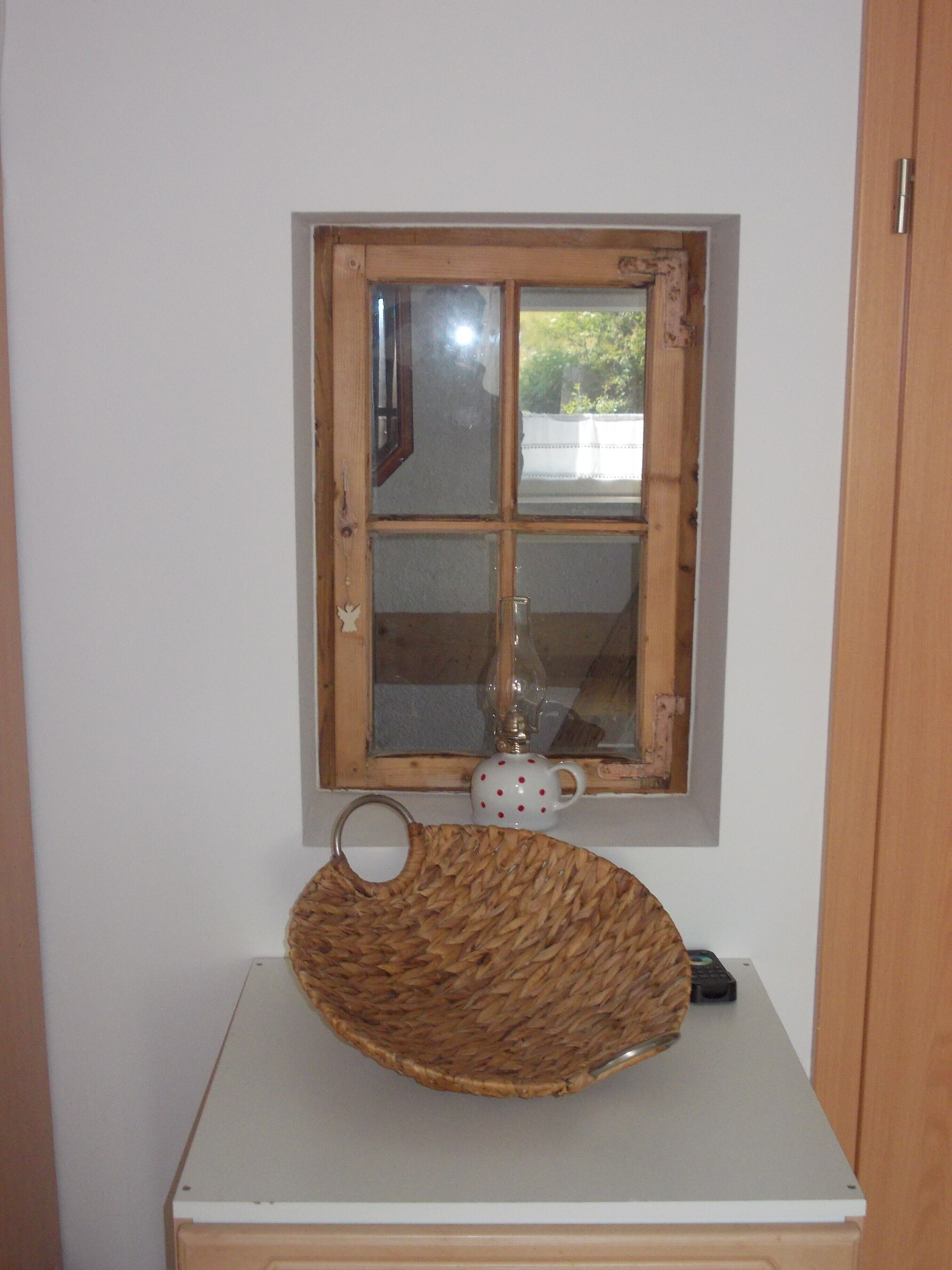Una stanza con una piccola finestra, un cesto di vimini su un tavolo bianco e una tazza a pois.