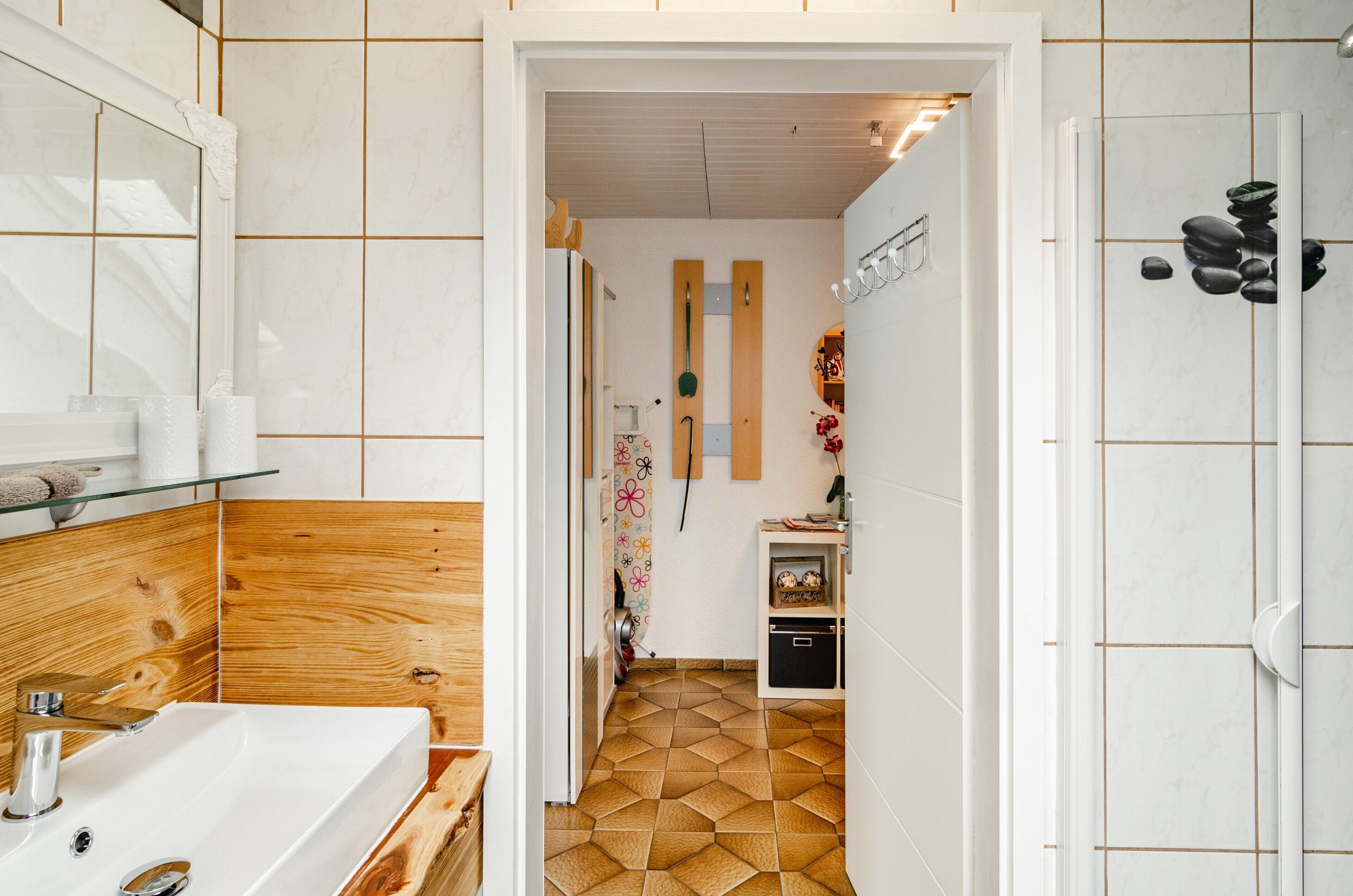 Une salle de bain avec un meuble-lavabo en bois, un lavabo blanc, un miroir et un espace douche doté d’un sol carrelé.