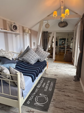 Ein Schlafzimmer mit einem Bett, Kissen, einem Nachttisch, einer Uhr, einer Pendelleuchte und Blick in die Küche.