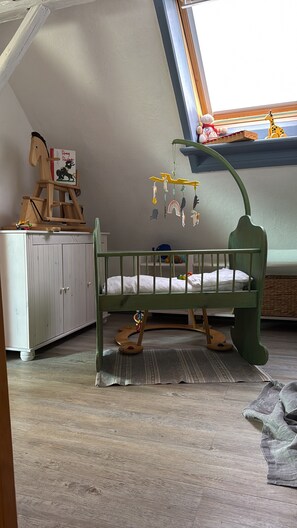 Ein Kinderzimmer mit einem grünen Kinderbett, einem hölzernen Schaukelpferd und einem Fenster mit Ausblick.