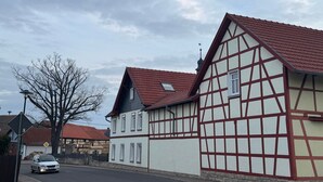 Une maison traditionnelle à colombages avec un toit rouge, un ciel dégagé et une voiture garée dans la rue.