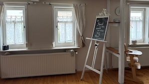 Une pièce avec un radiateur, deux fenêtres avec des rideaux, un tableau noir avec du texte et une chaise en bois.