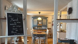 Une pièce avec un plancher en bois, une table à manger avec des chaises, un buffet bleu et un tableau noir avec du texte.