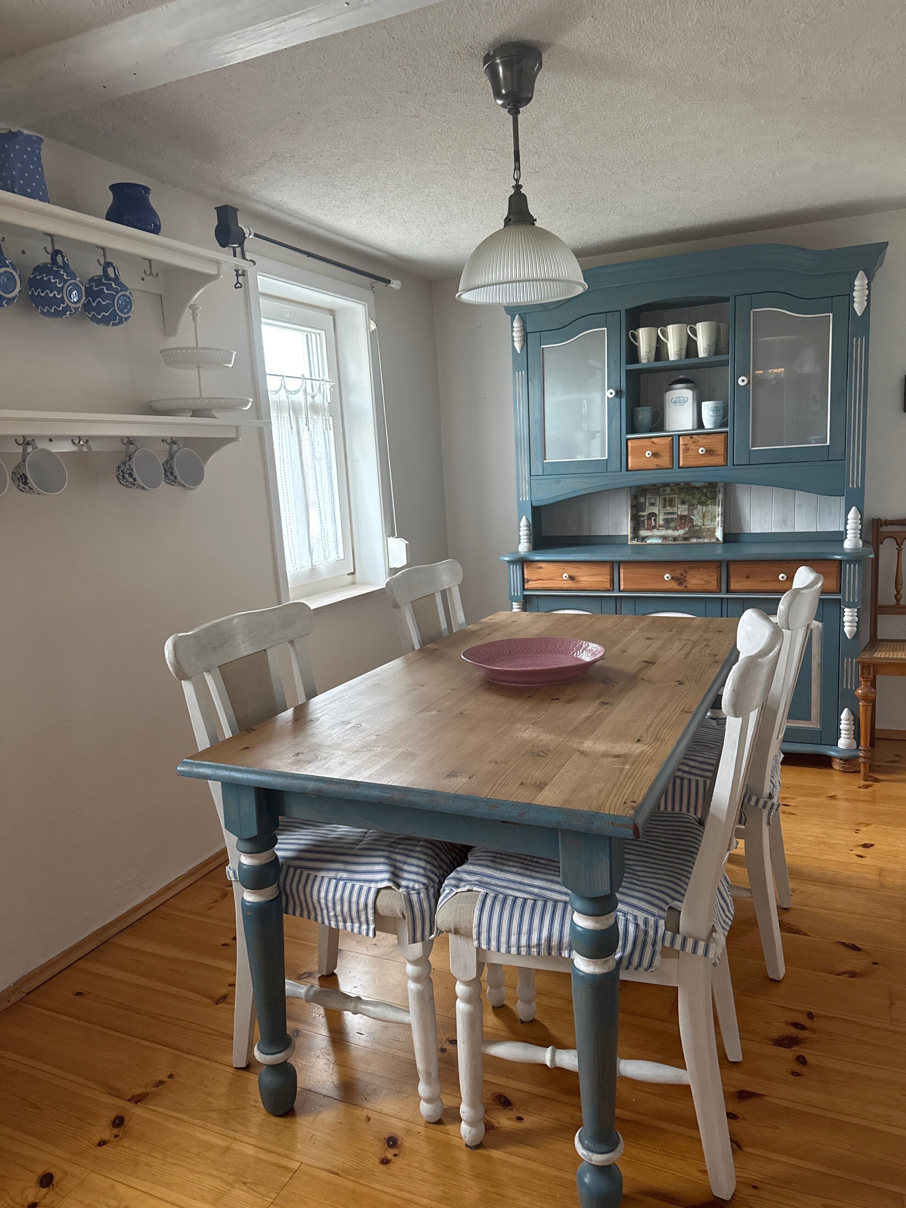 A dining room with a wooden table, white chairs, a blue cabinet with glass doors, and a hanging light fixture.