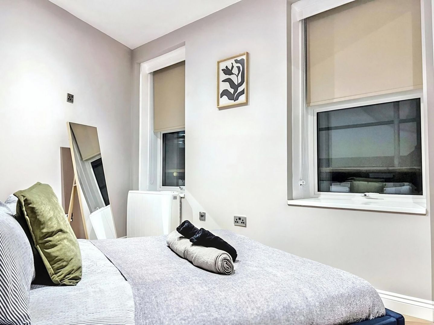 A bedroom with a bed, a radiator, a window, and a wall-mounted picture.
