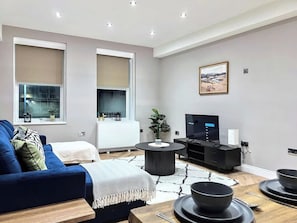 A modern living room with a sofa, a TV, and a dining area with plates and bowls.