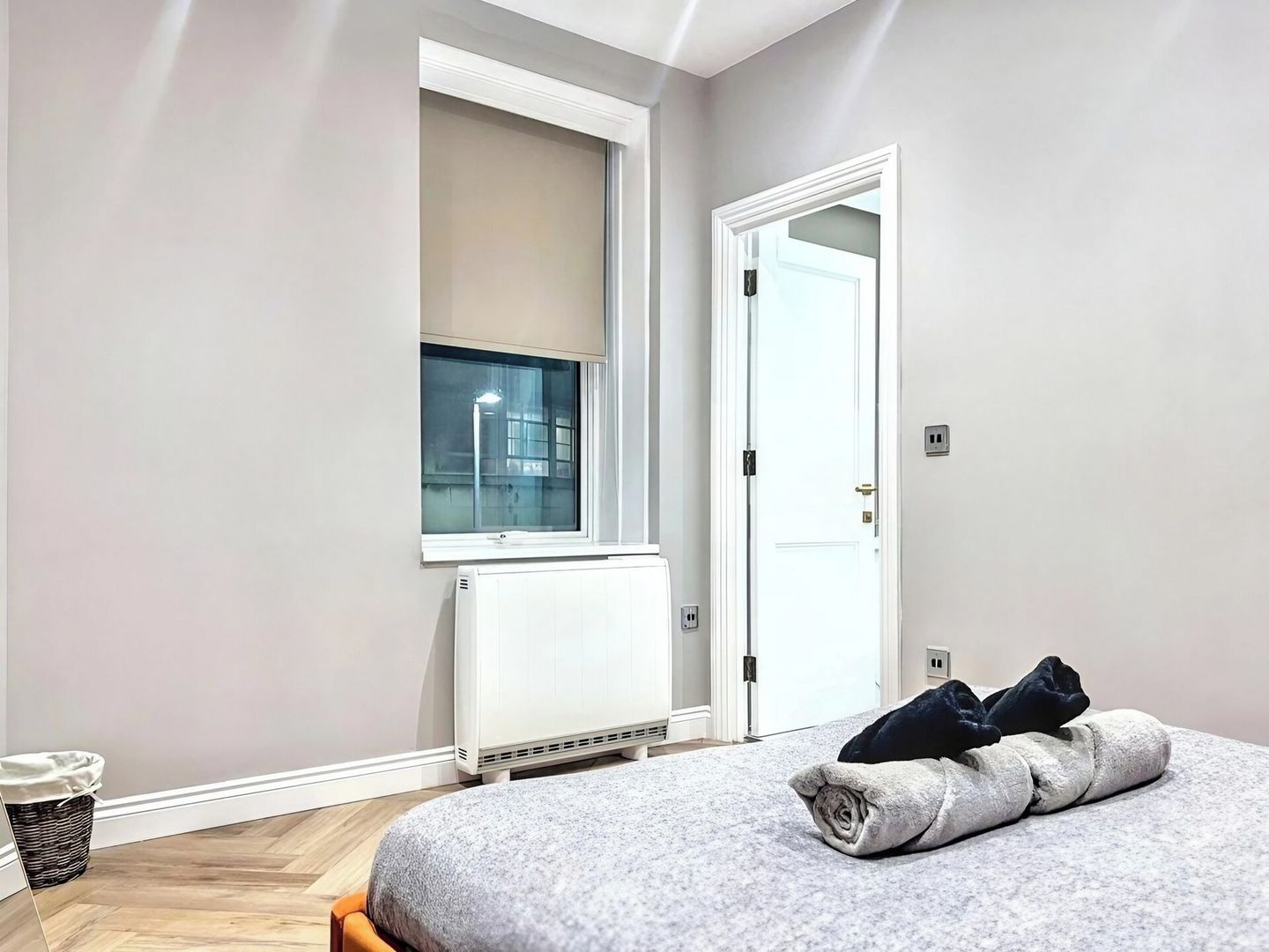 A bedroom with a bed, a radiator, a window, and a door.