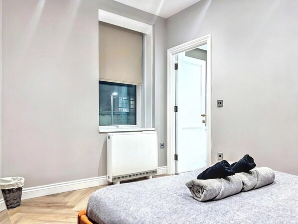 A bedroom with a bed, a radiator, a window, and a door.