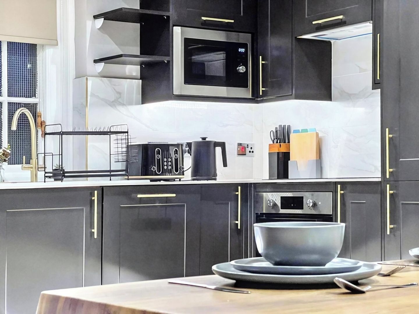 Une cuisine moderne avec des meubles de couleur sombre, un four à micro-ondes, un grille-pain et un bol posé sur le plan de travail.