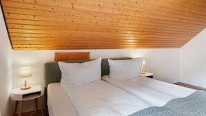 A room with a sloped ceiling, a bed with white bedding, two bedside tables with lamps, and a wooden headboard. - Apartment 'Glashütte' with Mountain View, Balcony and Wi-Fi (Sankt Märgen)