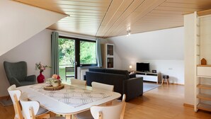 A modern living room with a dining table, chairs, a sofa, and a TV. - Apartment 'Glashütte' with Mountain View, Balcony and Wi-Fi (Sankt Märgen)