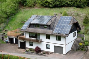 A two-story house with solar panels on the roof, a garage, and a small garden.