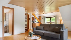 A modern living room with a grey sofa, wooden flooring, a small round table with a vase, and a staircase leading to an upper level. - Apartment 'Glashütte' with Mountain View, Balcony and Wi-Fi (Sankt Märgen)