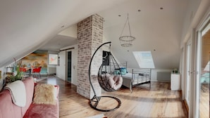 Ett rum i loftstil med ett sluttande tak, en tegelkolonn, en hängstol, en säng och en matplats med utsikt.