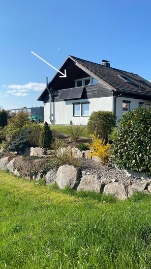 Una casa con tetto spiovente, pannelli solari e un giardino con rocce e piante.