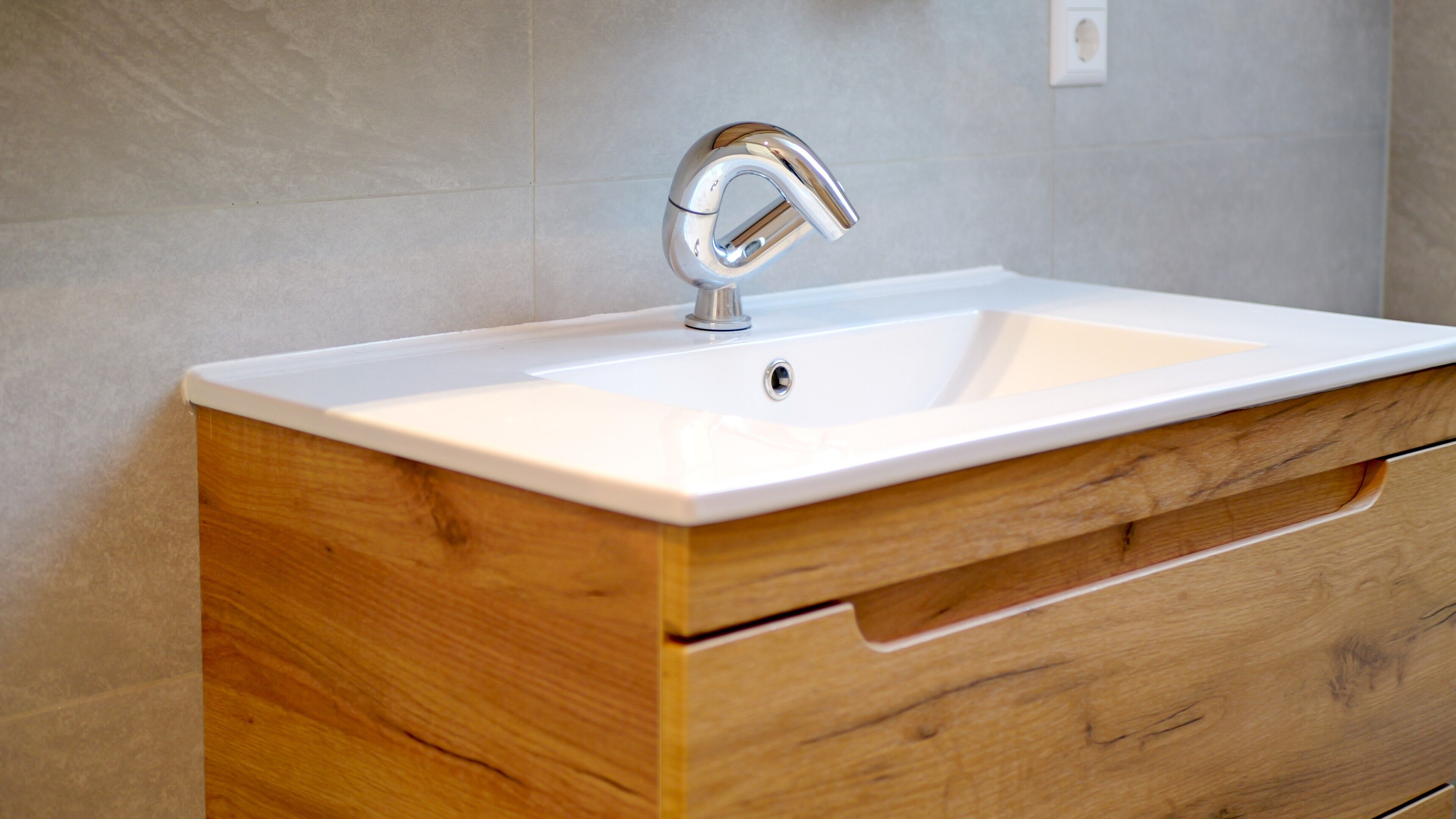 A bathroom with a white sink, wooden vanity, and a chrome faucet.